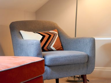 A grey armchair with a patterned cushion next to an orange upholstered ottoman at Riverside Park 6 in Keswick