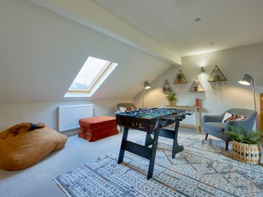 A room with a foosball table a bean bag chair an orange ottoman two armchairs and triangular wall shelves at Riverside Park 6 in Keswick