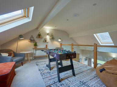 A loft room with a foosball table a grey armchair and a desk with wall shelves at Riverside Park 6 in Keswick