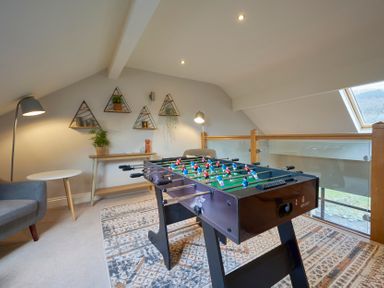 A loft room with a foosball table a gray armchair a side table a console table with plants and lamps Riverside Park 6 Keswick
