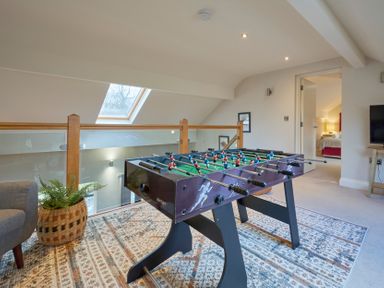 A game room with a foosball table on a patterned rug next to a gray chair and a plant basket at Riverside Park 6 in Keswick
