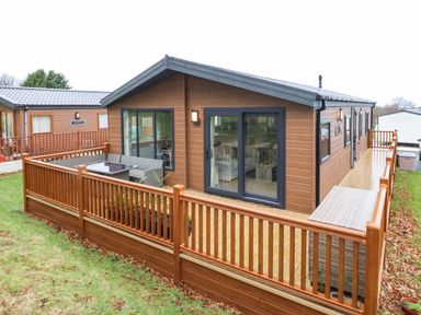 A wooden cabin with a fenced deck and outdoor seating in a grassy area at Woodpecker Lodge in Dunbar