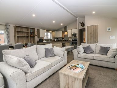 A living room with two sofas and a wooden coffee table with magazines and a kitchen with cabinets and appliances at Woodpecker Lodge in Dunbar