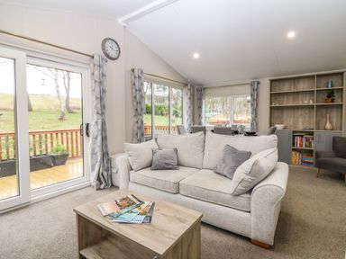 A living room with a beige sofa and a wooden coffee table with magazines at Woodpecker Lodge in Dunbar