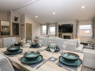 A dining table set with plates bowls and glasses in a living room with sofas and a television at Woodpecker Lodge in Dunbar