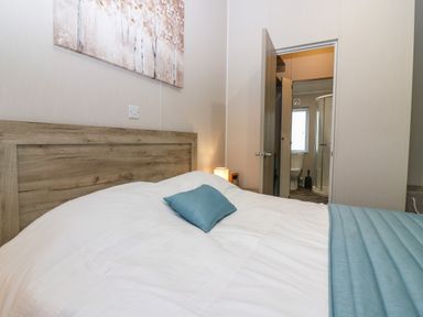 A bedroom with a wooden headboard a white bedspread and blue pillow and a view into a bathroom at Woodpecker Lodge in Dunbar