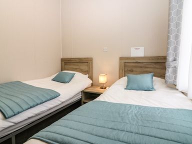 A bedroom with two single beds with blue bed runners and pillows separated by a nightstand with a lamp at Woodpecker Lodge in Dunbar