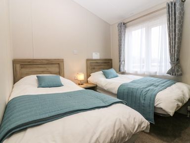 A bedroom with two single beds with blue throws and pillows and a window with curtains at Woodpecker Lodge in Dunbar
