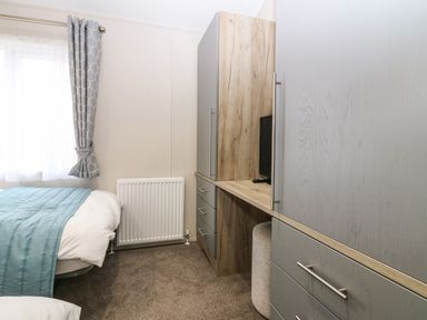 A bedroom with a single bed near a window with curtains and a built in wardrobe with drawers and a small tv at Woodpecker Lodge in Dunbar