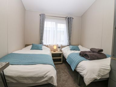 A bedroom with two single beds blue pillows and blankets a nightstand with a lamp and curtains at Woodpecker Lodge in Dunbar