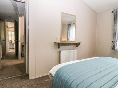 A bedroom with a bed covered by a blue blanket a wall mirror above a wooden shelf and a window with gray curtains at Woodpecker Lodge in Dunbar