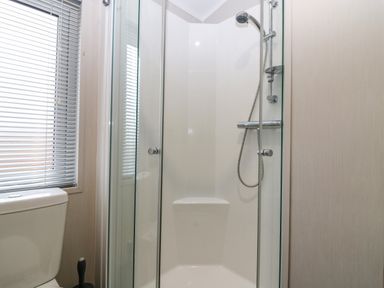 A bathroom with a shower enclosure a toilet and window blinds at Woodpecker Lodge in Dunbar