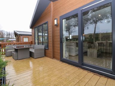 An outdoor wooden deck with a gray wicker dining set and sliding glass doors leading to a living room at Woodpecker Lodge in Dunbar