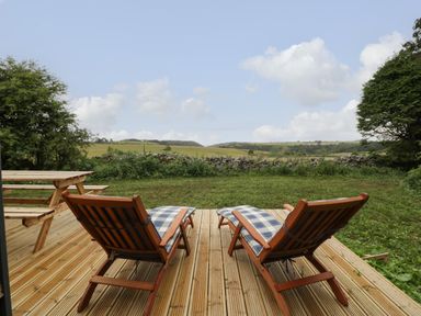 Two wooden lounge chairs with cushions on a deck facing a grassy yard and fields beyond at Lime Kiln in Blagdon
