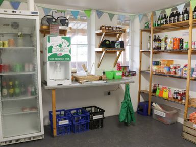 A room with shelves of bottled drinks and groceries and a milk dispenser at Lime Kiln Blagdon