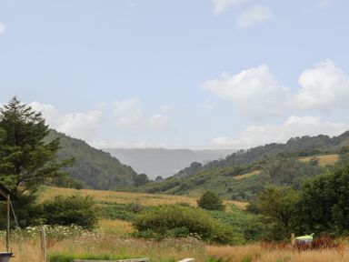 A rural landscape with grassy fields hills and scattered trees under a partly cloudy sky at Lime Kiln in Blagdon