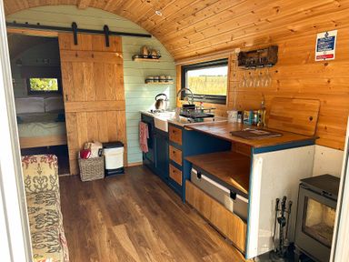 A compact kitchen with wooden cabinets and a small stove next to a bedroom with a sliding wooden door at Lime Kiln in Blagdon