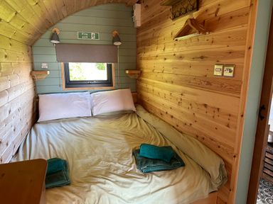 A bedroom with a double bed two white pillows a small window and wooden walls at Lime Kiln in Blagdon