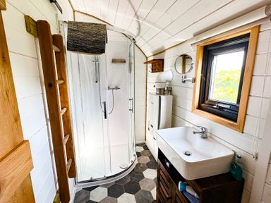 A bathroom with a curved glass shower, towel rack, sink, window, and wooden cabinet at Lime Kiln in Blagdon