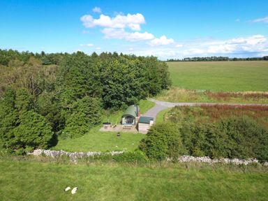A small cabin with a green roof near a forest and open fields at Lime Kiln in Blagdon
