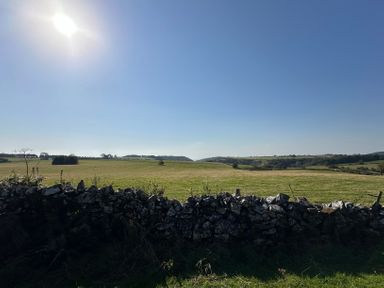 A grassy field with a stone wall in the foreground and hills in the distance under a clear sky at Lime Kiln in Blagdon