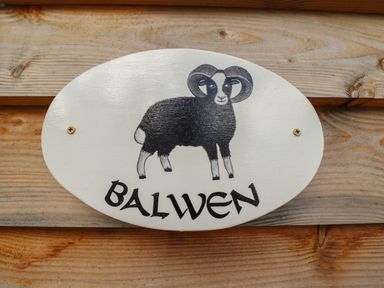 A wooden sign with a drawing of a black and white ram and the word Balwen attached to wood at Balwen Shepherd's Hut in Berriew