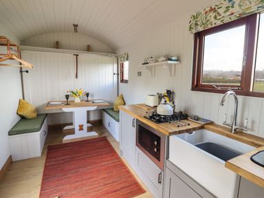 A kitchen and dining area with wooden countertops a gas stove a sink a small dining table with two cushioned benches and a red rug at Balwen Shepherd's Hut in Berriew