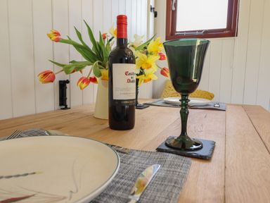 A dining table set with a wine bottle flowers plates and green glasses at Balwen Shepherd's Hut in Berriew