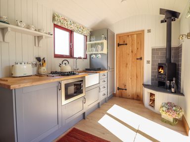 A kitchen with wood countertops a stove toaster and a wood burning stove near a wooden door at Balwen Shepherd's Hut in Berriew