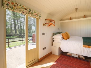 A bedroom with a bed orange cushions a red rug and a door leading outside at Balwen Shepherds Hut in Berriew