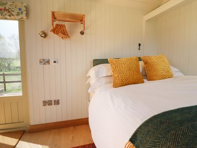 A bedroom with a bed with yellow pillows and white sheets next to a door and wooden hangers on the wall at Balwen Shepherd's Hut in Berriew