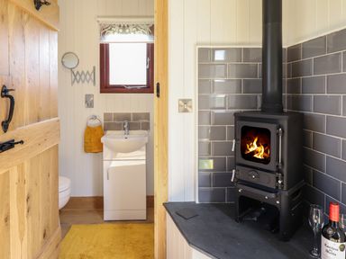 A small bathroom with a sink and towel next to a black wood stove with a fire inside at Balwen Shepherd's Hut in Berriew