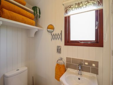 A bathroom with a white sink a mirror window orange towels and a toilet at Balwen Shepherd's Hut in Berriew