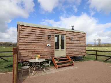 A wooden shepherd's hut with stairs leading to double doors and a metal table with two chairs outside in a field at Balwen Shepherd's Hut in Berriew