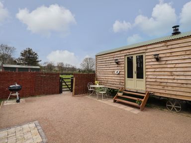 An outdoor area with a wooden hut on wheels a small table with two chairs a barbecue grill and a gate at Balwen Shepherd's Hut in Berriew
