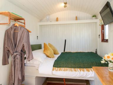 A bedroom with a bed two pillows a green blanket and a hanging robe at Balwen Shepherd's Hut in Berriew