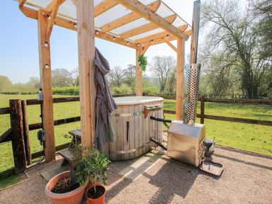 An outdoor hot tub with a wooden frame roof and a heating stove in a fenced garden at Balwen Shepherd's Hut in Berriew