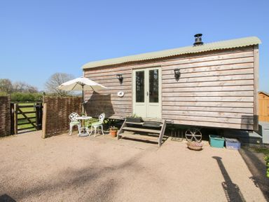 An outdoor area with a wooden shepherd's hut a small table with two chairs and an umbrella at Balwen Shepherd's Hut in Berriew