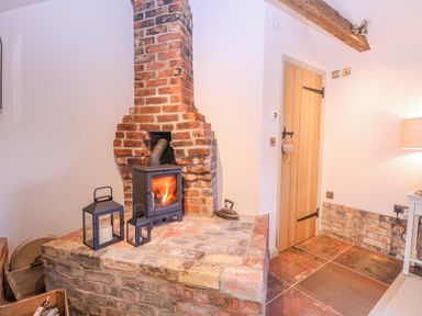 A brick fireplace with a wood burning stove and two lanterns next to a wooden door and a lamp at The Forge in Old Newton near Stowmarket