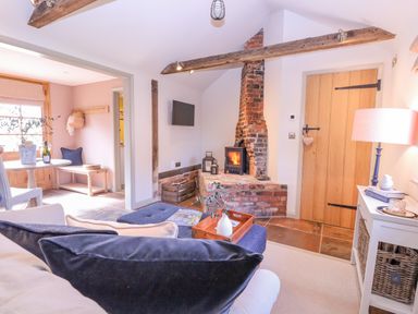A living room with a wood burning stove exposed brick chimney wooden beams and a seating area at The Forge in Old Newton near Stowmarket