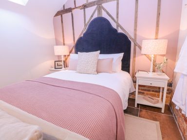 A bedroom with a bed covered with a pink blanket and two bedside tables with lamps at The Forge in Old Newton near Stowmarket