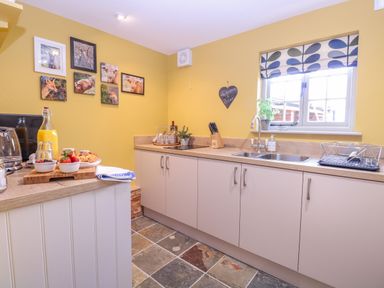A kitchen with yellow walls white cabinets stone tile floor and framed animal pictures at The Forge in Old Newton near Stowmarket