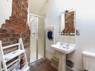 A bathroom with a shower cubicle sink toilet mirror towel rack and exposed brick wall at The Forge in Old Newton near Stowmarket