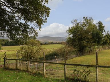 A rural field with trees and a wooden fence with hills in the distance at Row End farm in Brough