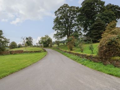 A curved paved road with grass and stone walls on each side and trees in the background at Row End farm in Brough