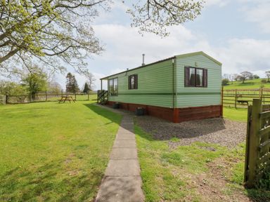 A green mobile home with a pathway leading to it and a picnic table in a grassy yard at Row End farm in Brough