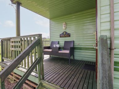 A porch with wooden railing and two chairs with a small table at Row End farm in Brough