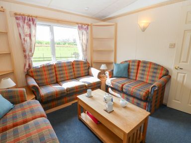A sitting room with patterned sofas a wooden coffee table with mugs and teapot and windows showing a green field at Row End farm in Brough