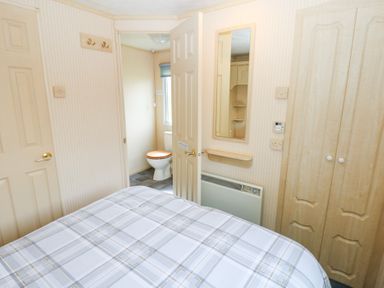 A bedroom with a bed covered in a plaid blanket a mirror on the wall a heater built in wooden wardrobes and a door open to a bathroom with a toilet at Row End farm in Brough