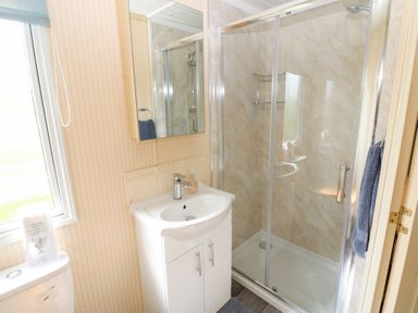A bathroom with a shower enclosure a white sink with cabinet a mirror and a toilet at Row End farm in Brough